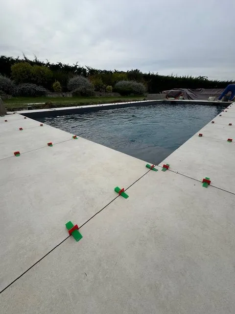 Carrelage clair en cours de pose tout autour de la piscine remplie