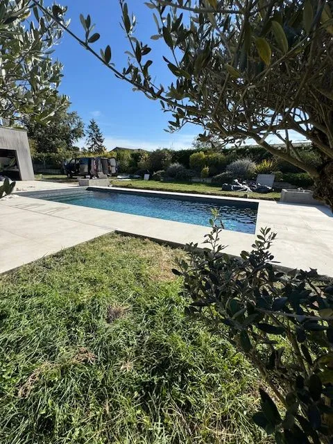 Vue de la piscine entourée de carrelage clair depuis le jardin