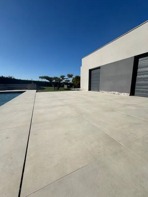 Large plage de piscine en carrelage clair devant la façade